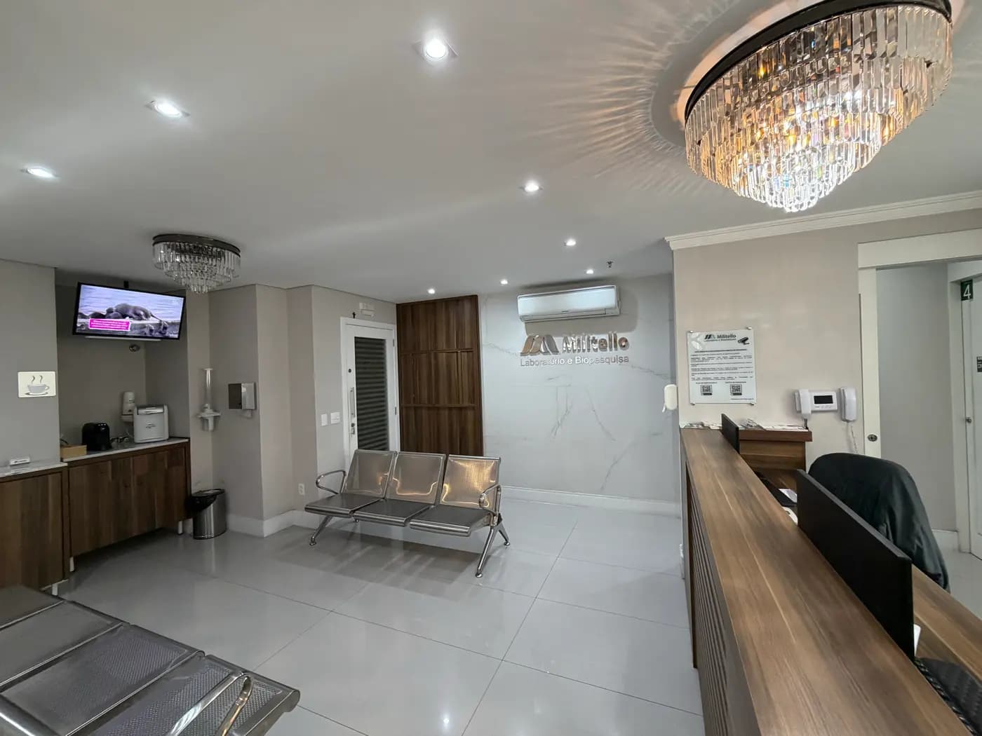 Sala de espera do laboratório, com televisão e lustre de cristal